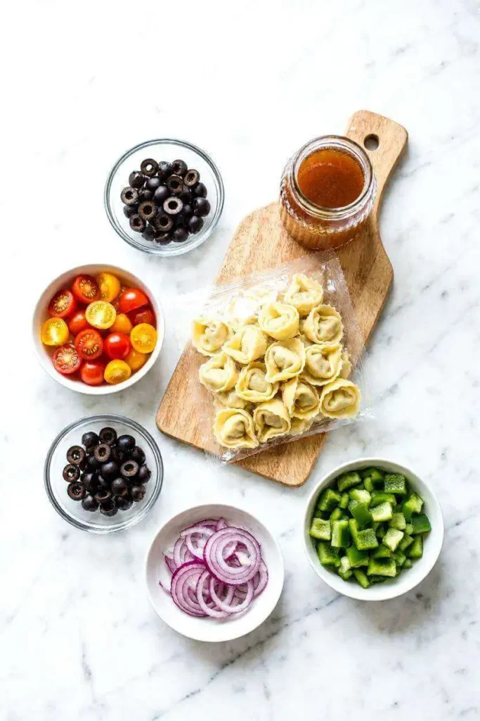 The Best Tortellini Cold Pasta Salad (Ready in 20 Minutes!) 3 All ingredients for tortellini cold pasta salad arranged on white marble including tortellini, cherry tomatoes, olives, bell pepper, and Italian dressing