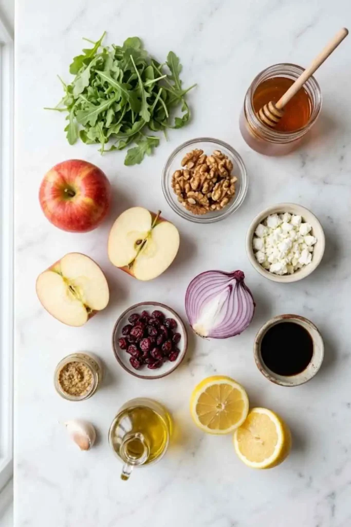 Easy Apple Arugula Salad - The Perfect Fall Flavor Combination! 2 Ingredients for Apple Arugula Salad Recipe including arugula, Honeycrisp apples, goat cheese, walnuts, and balsamic dressing on white marble