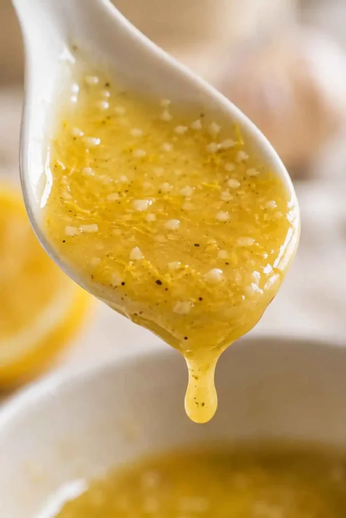 Lemon Garlic Vinaigrette Recipe – Bright, Bold & Done in 5 Minutes 4 Close-up of glossy lemon garlic vinaigrette coating the back of a ceramic spoon showing perfect thick emulsified texture